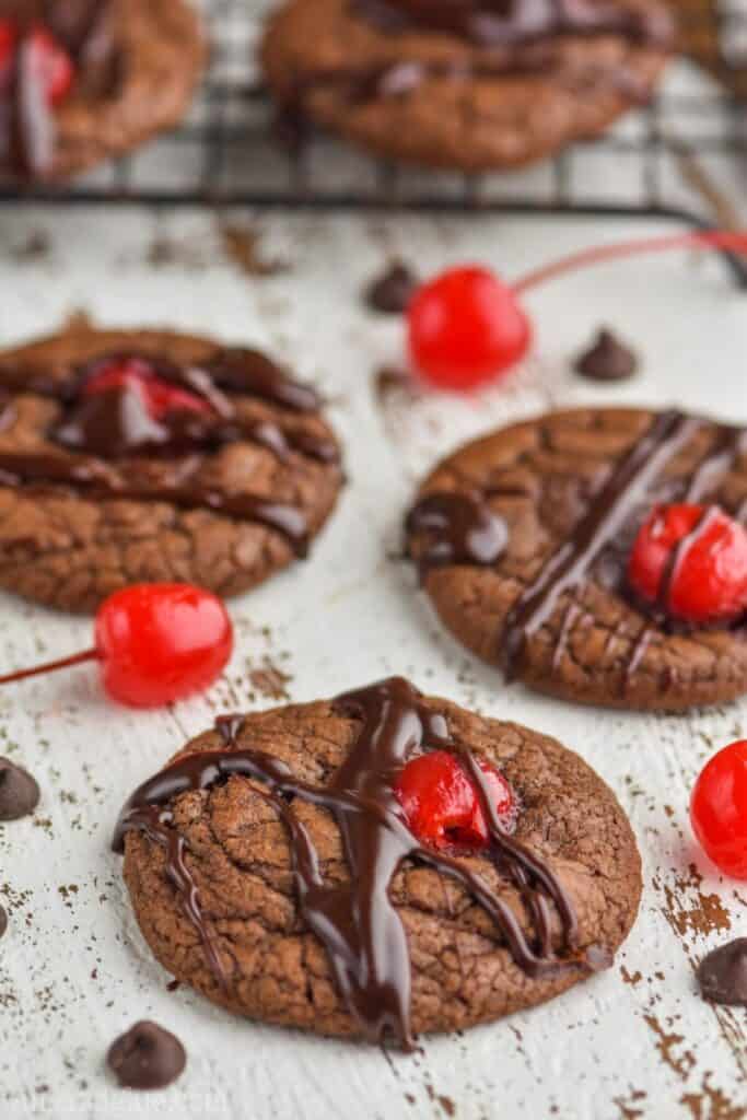several chocolate covered Cherry cookies on a wood board with the cooling rack in the background