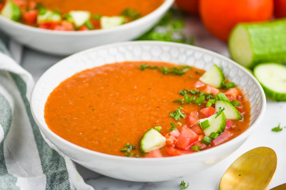 landscape view of gazpacho soup recipe in a white bowl garnished with fresh vegetables