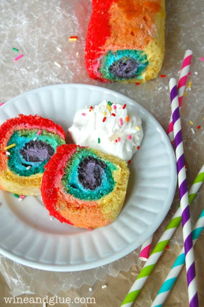 Slices of the Rainbow Cake Roll that is swirled with different colors and has a side of whip cream with sprinkles. 