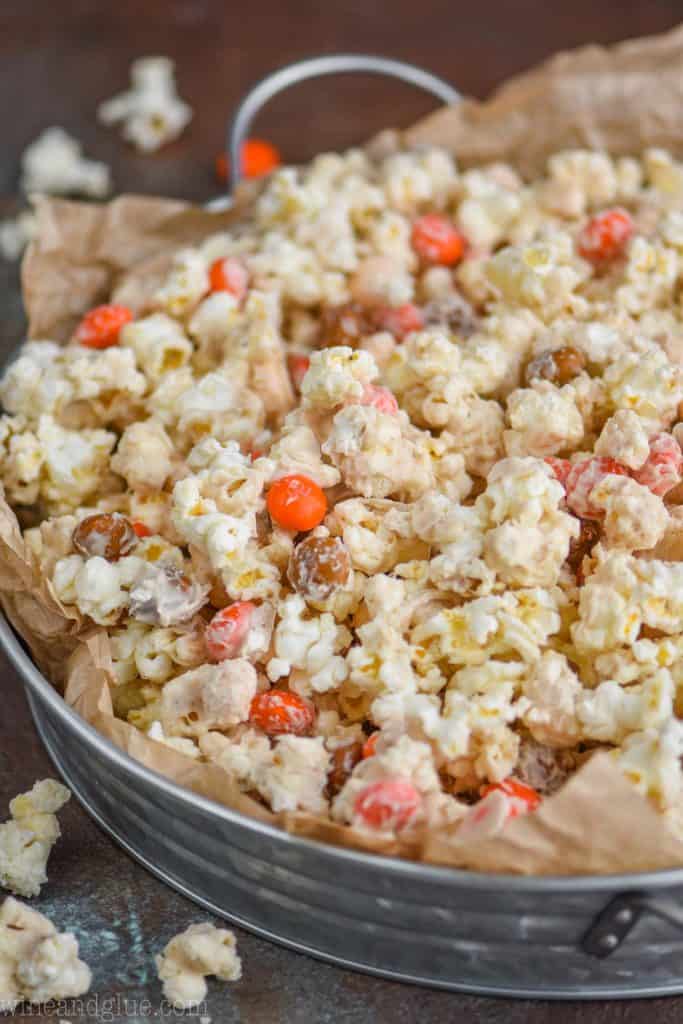 side view of a galvanized metal try lined with brown parchment paper and full of white chocolate popcorn recipe flavored with pumpkin spice