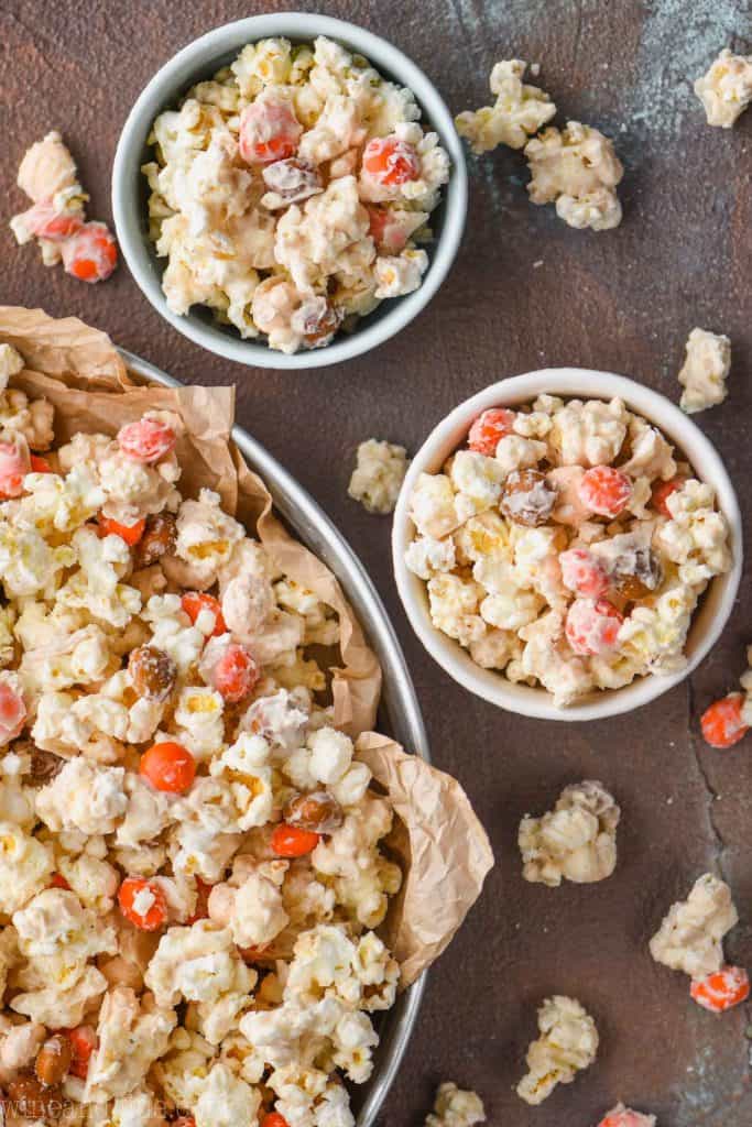 overhead view of two small bowls full of pumpkin spice popcorn recipe next to a larger tray full of the same recipe