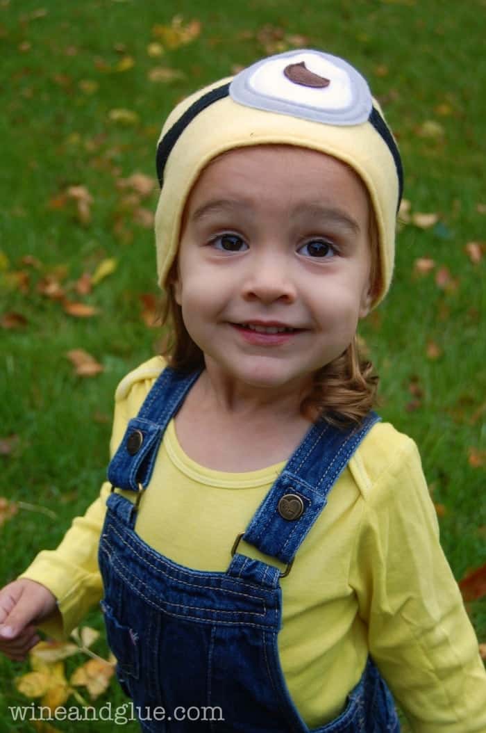 little girl in overalls wearing a minion hat