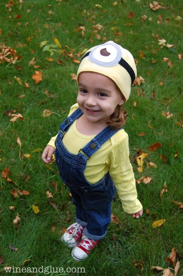 little girl in overalls, red shoes, yellow shirt and minion hat