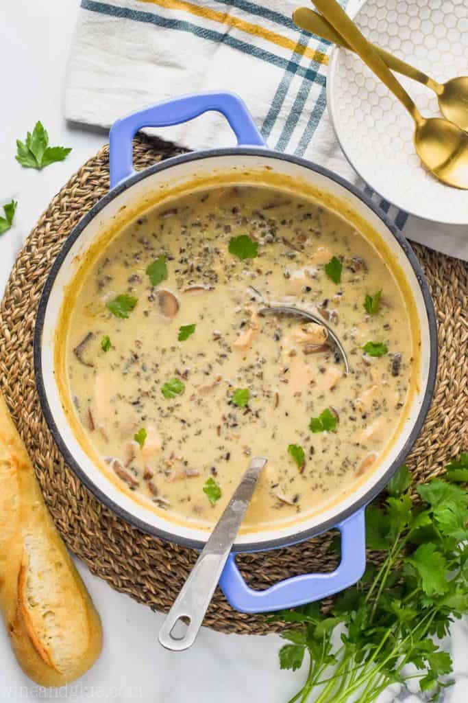 overhead view of a pot of creamy chicken wild rice soup recipe with a baguette and garnished with parsley