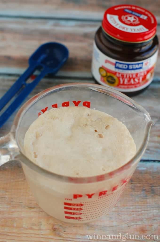 a glass pyrex measuring cup with with yeast that has grown and a bottle of active dry yeast in the background