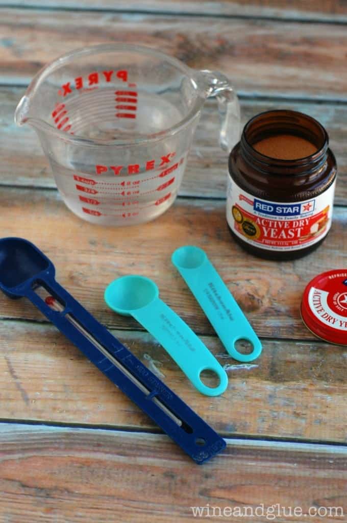 two measuring spoons, active dry yeast, a thermometer, and a measuring cup with warm water to make pizza dough