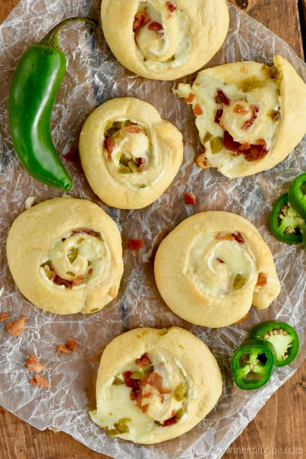 overhead view of six jalapeño popper pinwheels on a piece of wax paper, a full jalapeño and some jalapeño slices around it