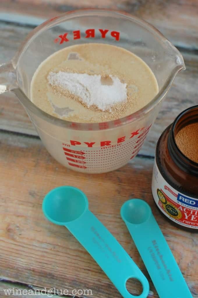 a small one cup measuring cup with water and yeast to start the best pizza dough