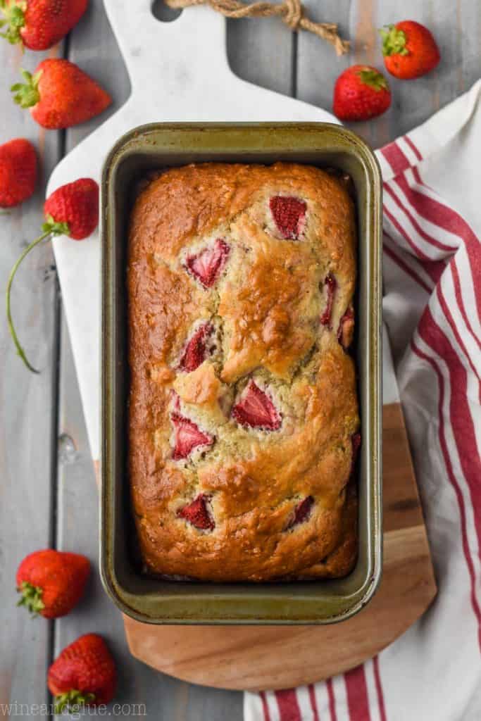 overhead view of strawberry banana bread in a loaf pan on a marble and wood cutting board with fresh strawberries around