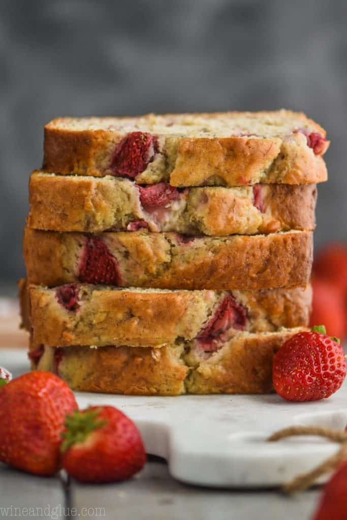 pieces of strawberry banana bread recipe stacked up on a marble cutting board against a dark background