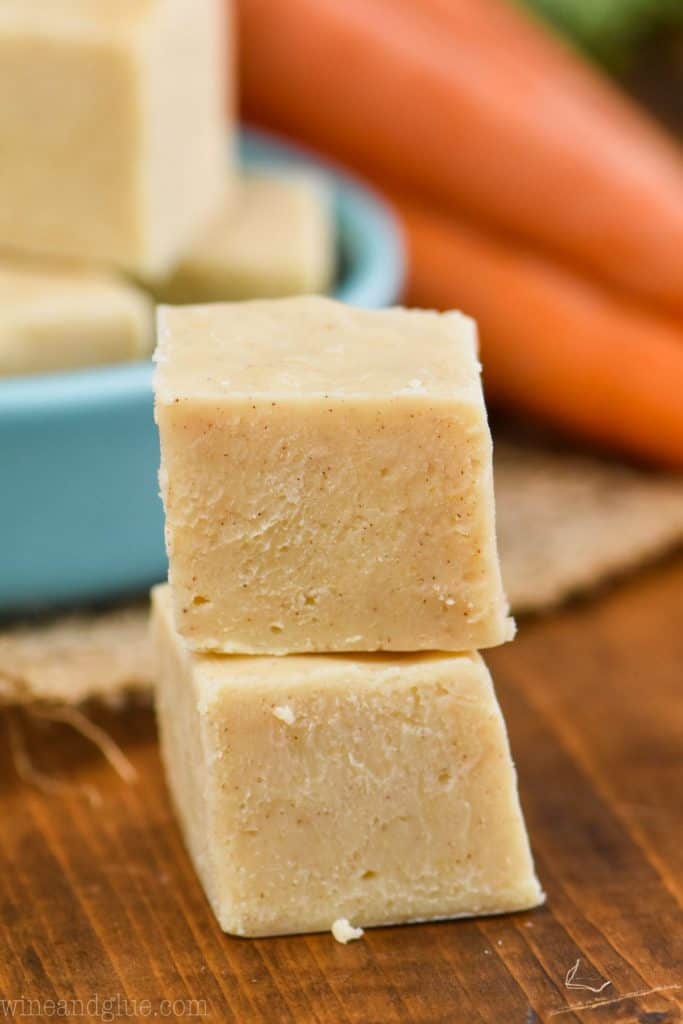two squares of carrot cake fudge on top of each other on a wood board