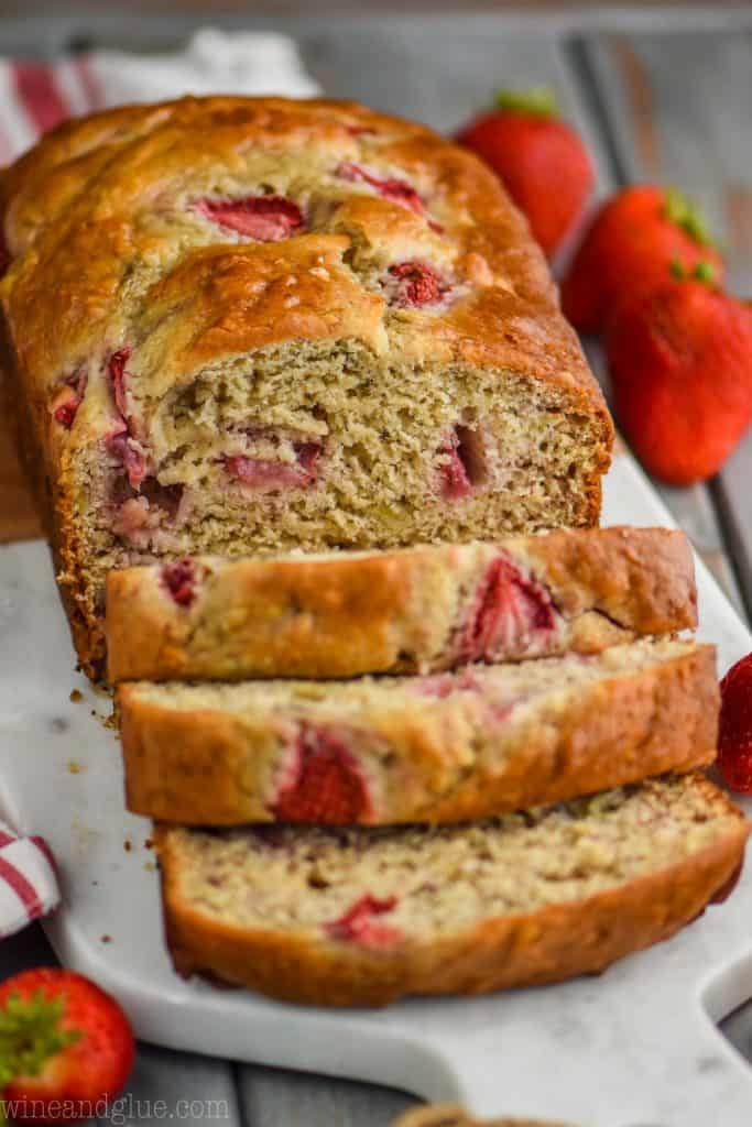 love of strawberry banana bread, sliced, on a marble cutting board with fresh strawberries around
