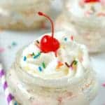 close up of a mason jar with no bake cheesecake, topped with a cherry, whipped cream and sprinkles, says no bake funfetti cheesecake cups