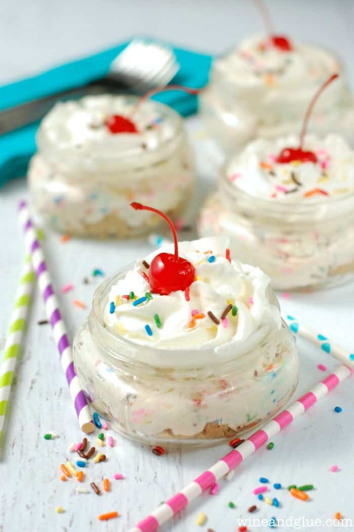 no bake cheesecake cups that are garnished with whipped cream, cherries, and sprinkles