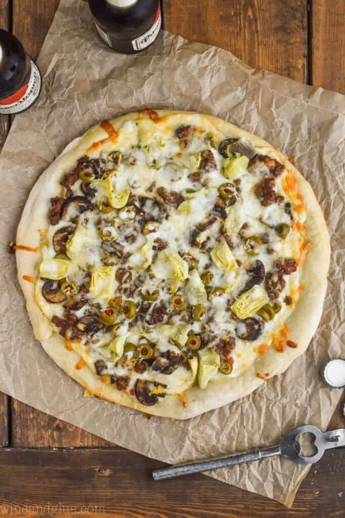 overhead view of a white pizza recipe on a piece of parchment paper with two beers next to it