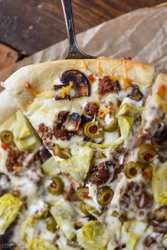 overhead view of a single piece of white pizza made with white pizza sauce being lifted up above the rest of the pizza