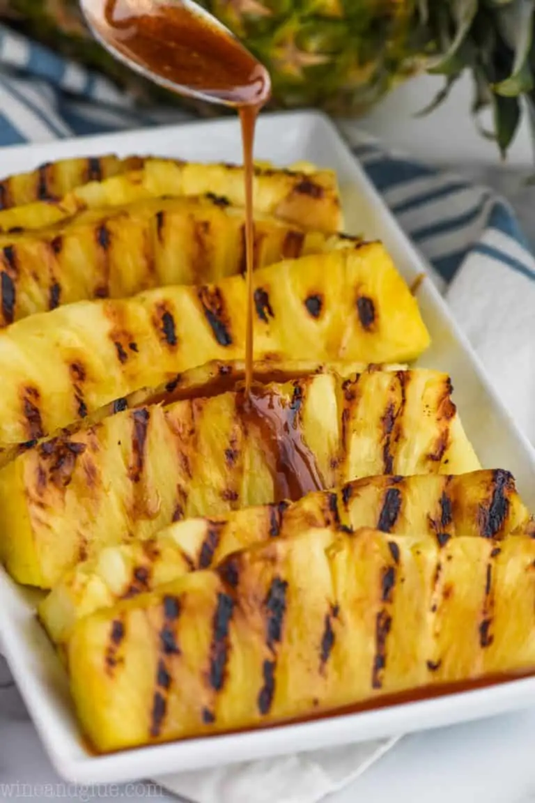 cinnamon honey drizzle being poured over a plate of grilled pineapple pieces