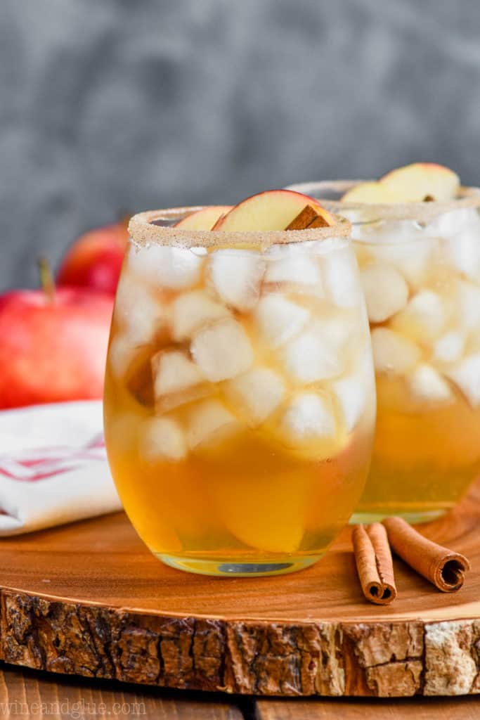 two glasses of the best apple margarita recipe on a wood tray with apples and cinnamon sticks