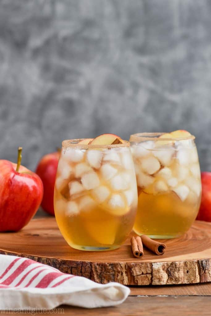 two glasses of the best apple margarita recipe on a wood tray with apples and cinnamon sticks