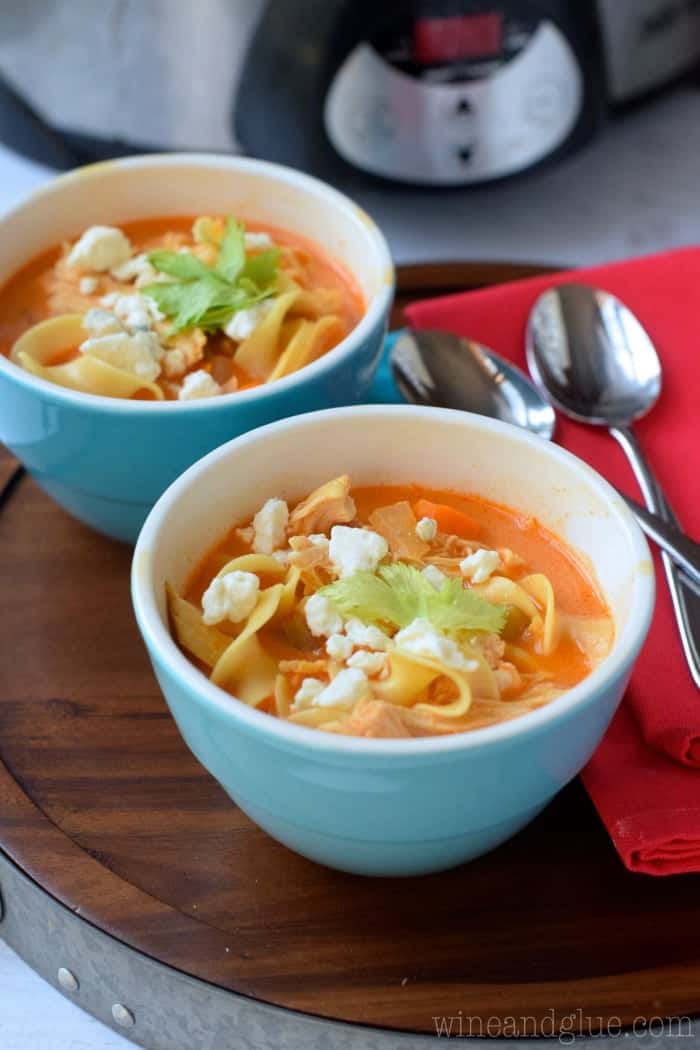 two blue bowls with buffalo chicken noodle soup in them, garnished with blue cheese