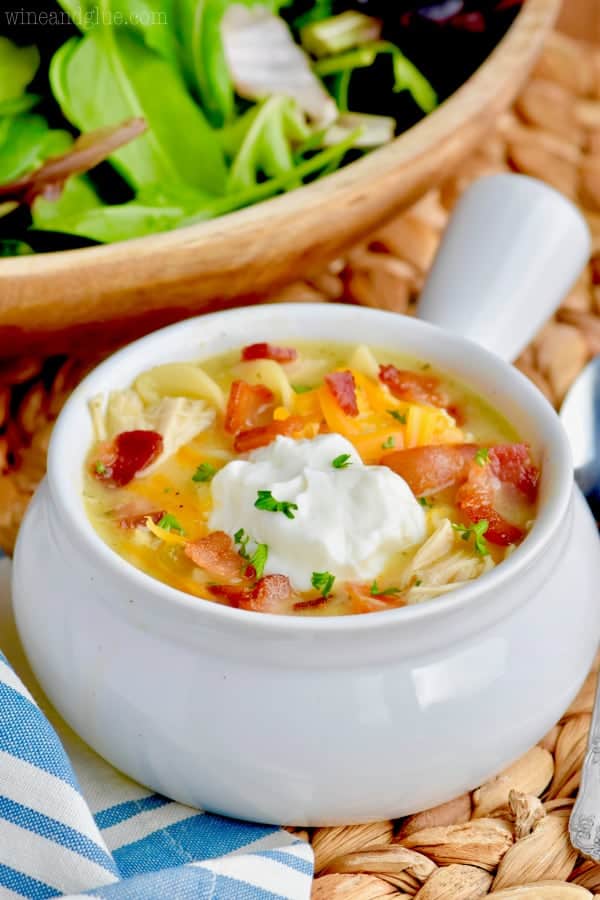 small white bowl with chicken noodle soup that has bacon in it and sour cream on top