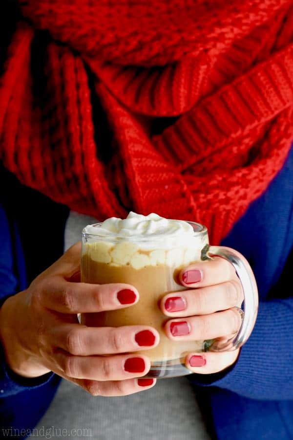 a woman holding a glass of eggnog latte topped with whipped cream