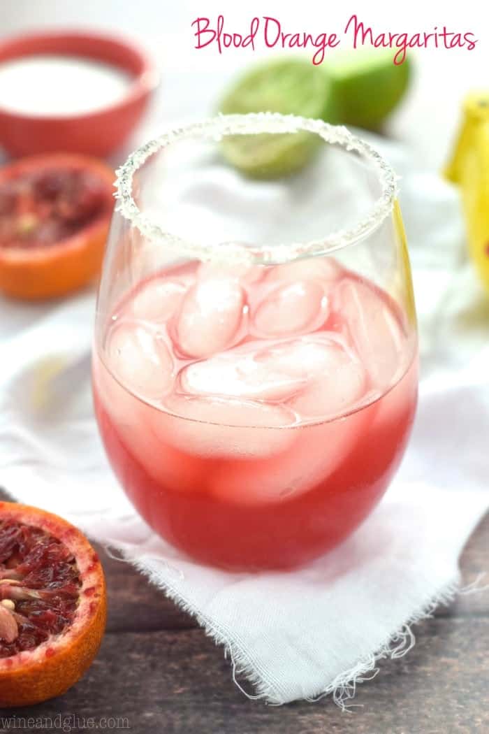 side view of a blood orange margarita in a stemless wine glass with a salted rim, says: blood orange margaritas