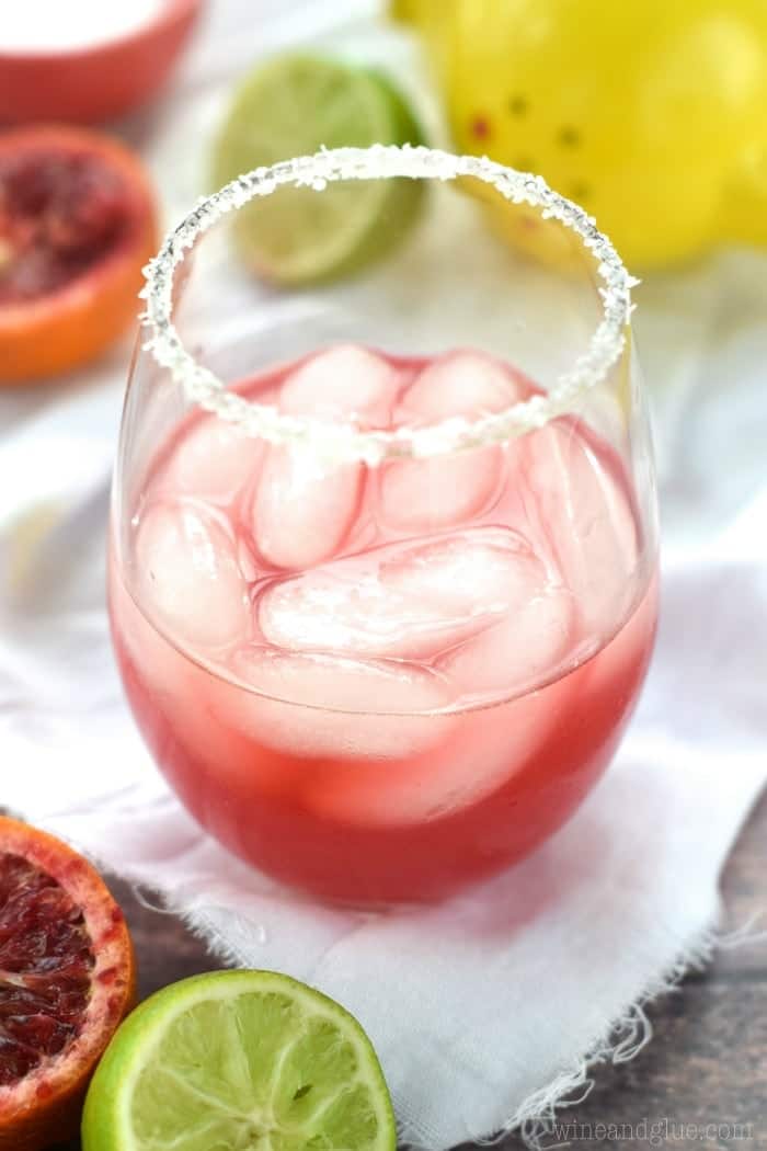 close up of a blood orange margarita in a stemless wine glass with a salt rim