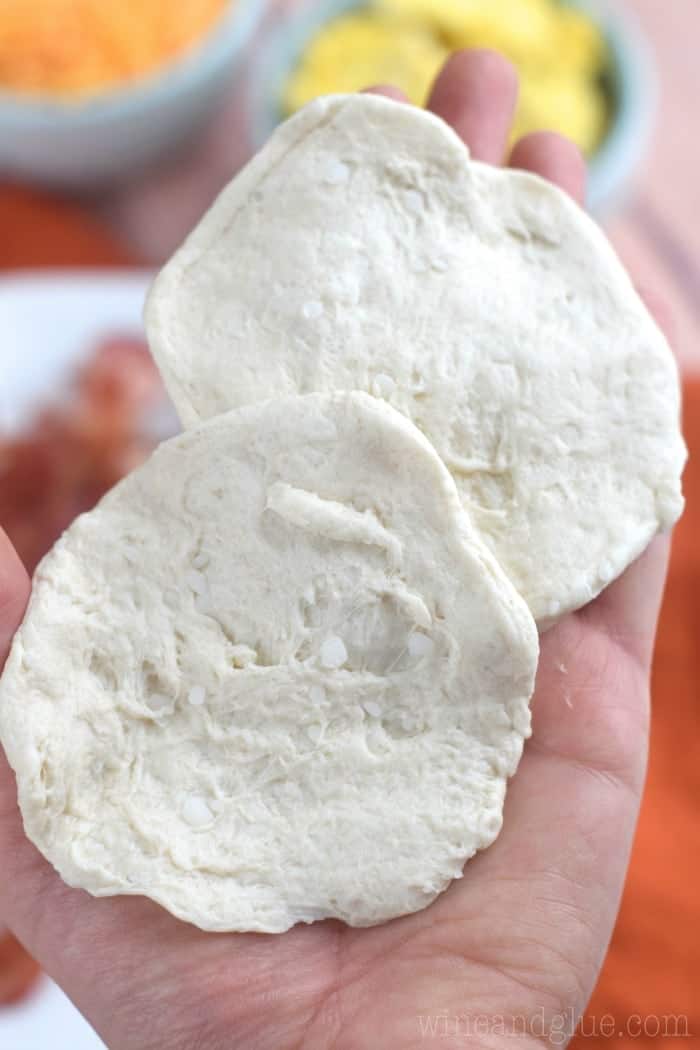 raw biscuits that have been cut in half and flattened in a woman's hand