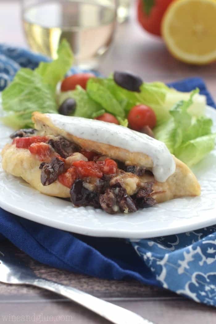 The Greek Stuff Chicken with a dollop of yogurt on top at one side of the plate. On the other side of the plate, is a salad with lettuce, olives, and cherry tomatoes. 