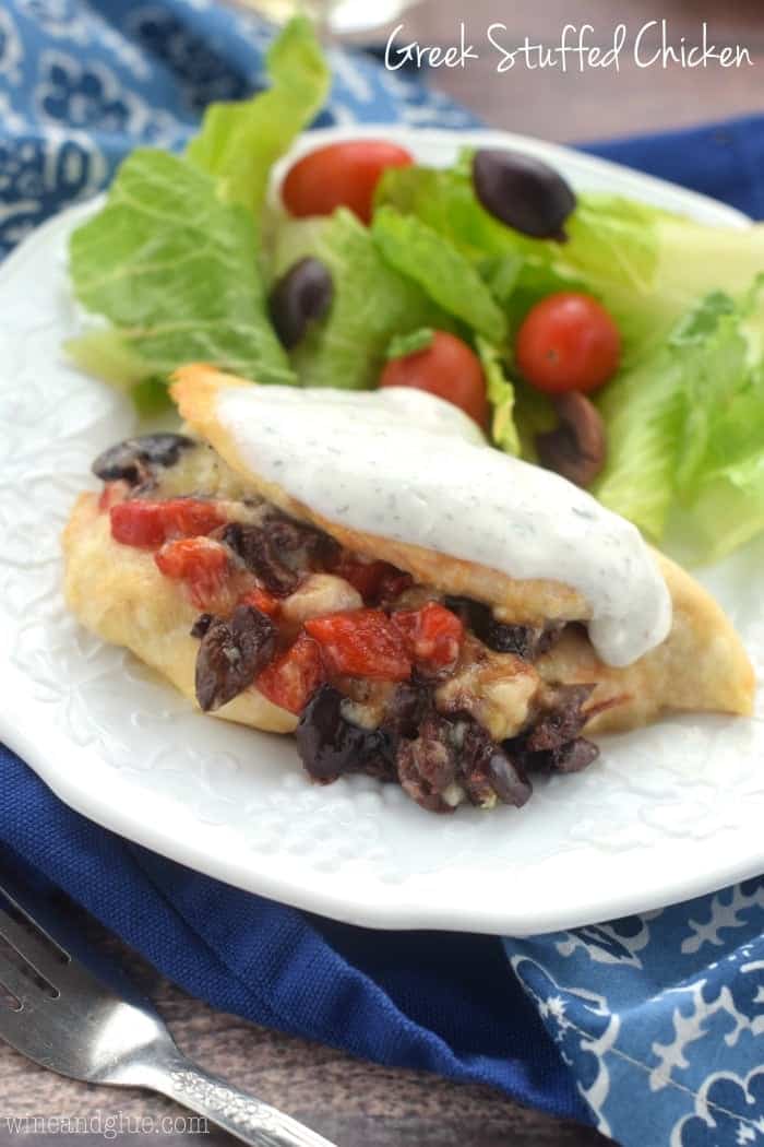 The Greek Stuff Chicken with a dollop of yogurt on top at one side of the plate. On the other side of the plate, is a salad with lettuce, olives, and cherry tomatoes. 