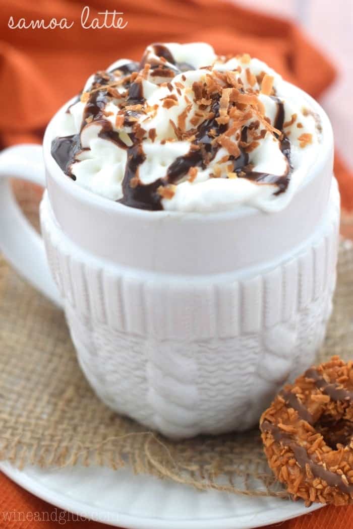 close up of a white mug with whipped cream on top, fudge drizzle, and toasted coconut, with Samoa cookies next to it, says: Samoa latte