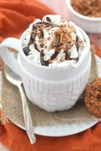 a small white mug full of a Samoa latte with whipped cream, chocolate drizzle and toasted coconut on top