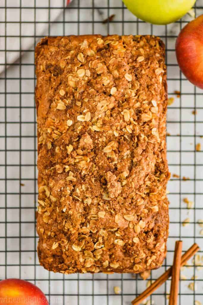 overhead view of apple bread that is covered in a streusel topping on a wire wrack with cinnamon sticks next to it