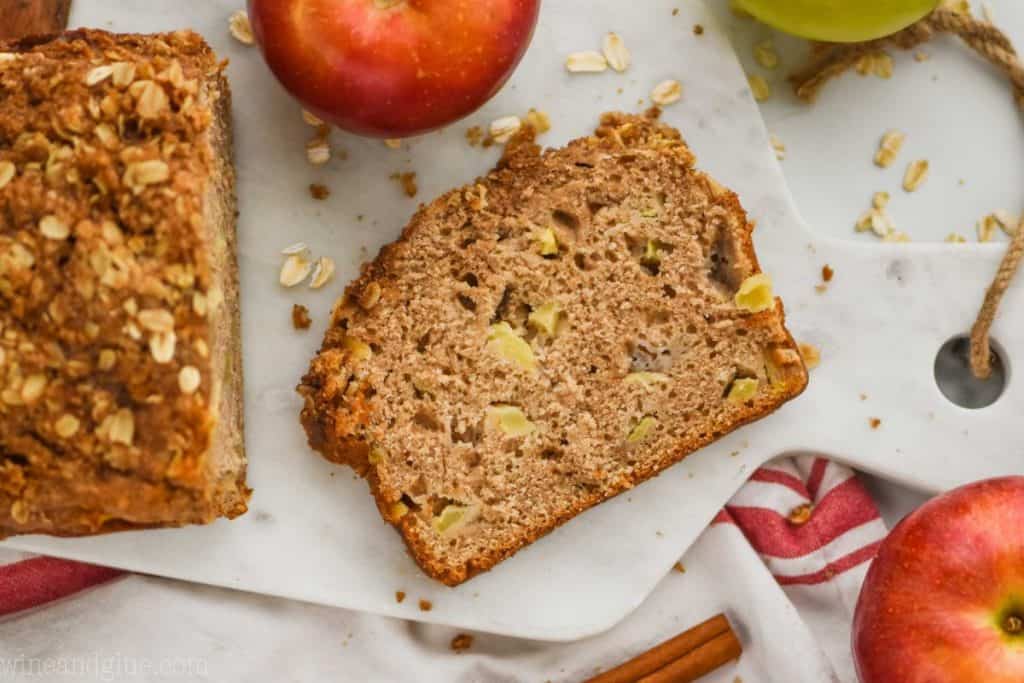 overhead view of a slice of easy apple bread recipe on a marble cutting board with oats around and fresh apples