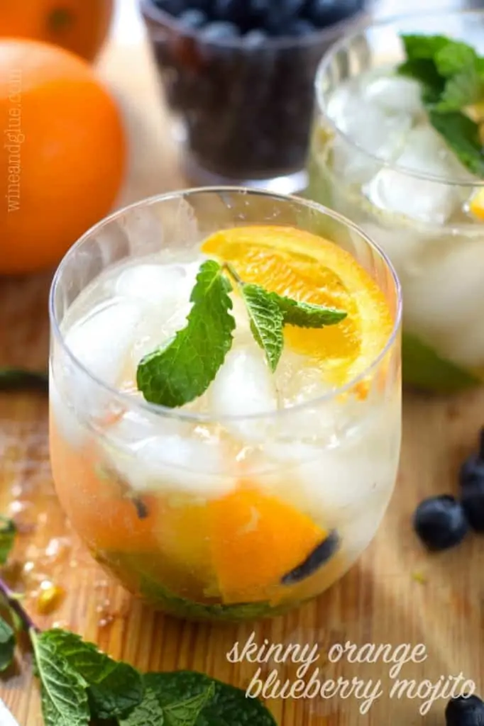 small glass filled with ice, mint, oranges, and blueberries, says: "skinny orange blueberry mojito"
