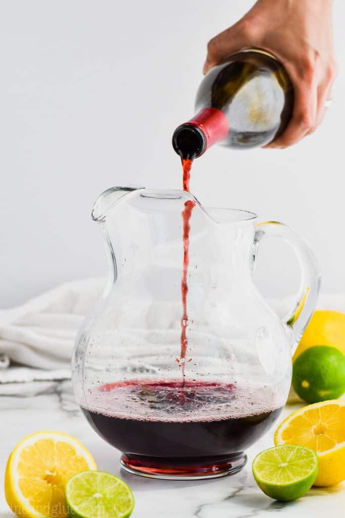 a bottle of red wine being poured into a pitcher to make classic red sangria recipe