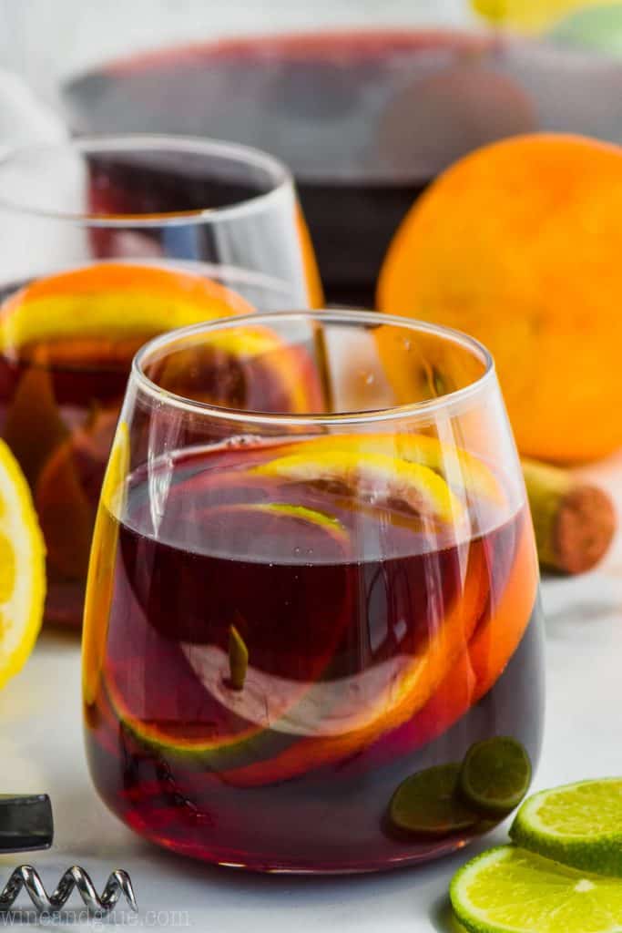glass of red wine sangria filled with slices of lime, lemon, and orange with another glass in the background