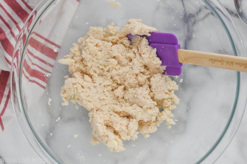 overhead view of pie crust dough after liquid has been added and it's being pulled together with a spatula