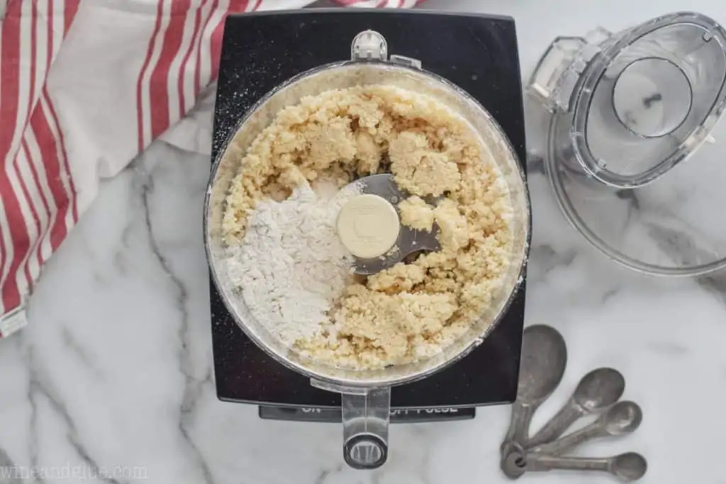 overhead of a food processor that has had cold butter and shortening added and now the last 1/2 cup of flour is poured on