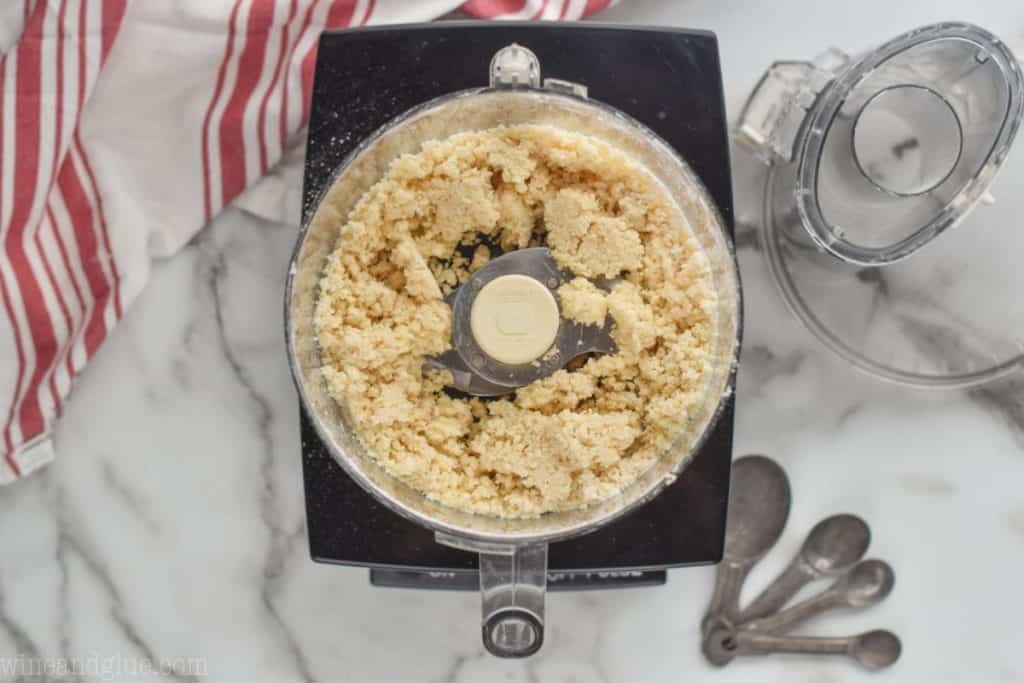 overhead of a food processor that flour and butter have been added to a flour mixture to blend together, mixture is crumbly with no flour showing