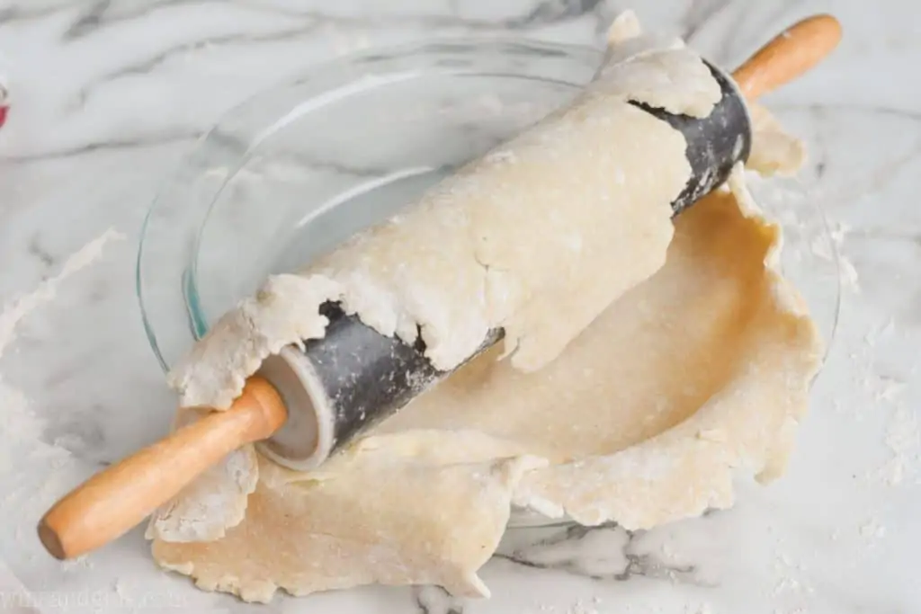 a pie crust being transferred to a pie pan using the rolling pin