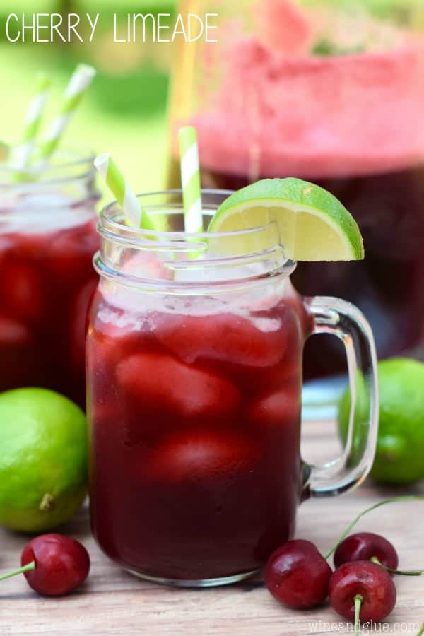 a glass of cherry limeade on a picnic table garnished with a lime wedge