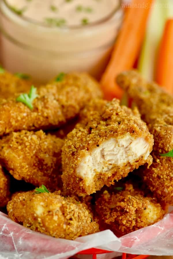 The Baked Chicken Tenders are piled in a basket and one of them is cut in half showing the tender and jucyu inside. 
