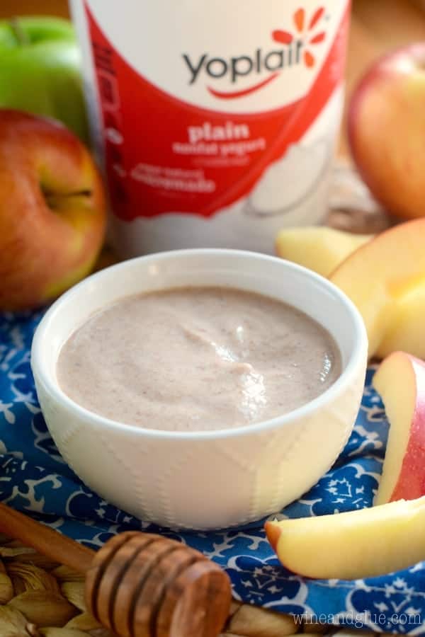 A small serving bowl with a smooth glossy brown dip surrounded by sliced apples