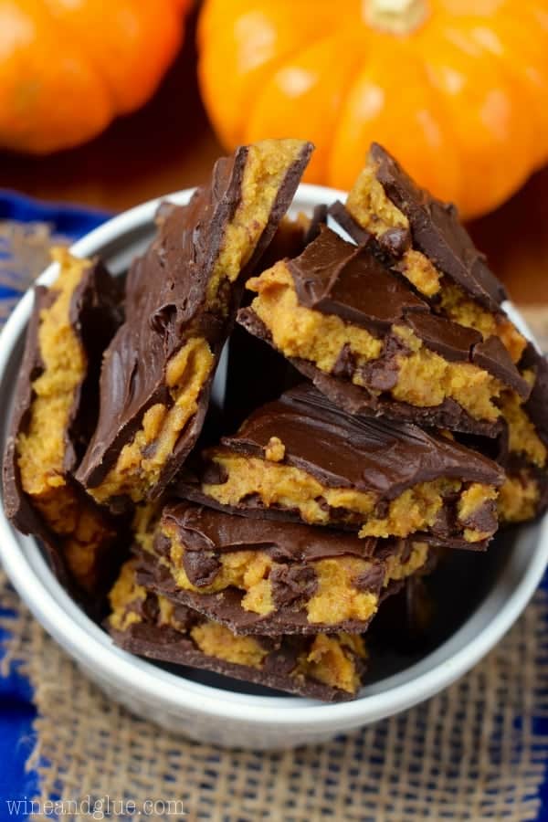 An overhead photo of the the Pumpkin Cookie Dough Bark in a ceramic bowl showing that the pumpkin cookie dough has chocolate chip cookies and wedged between two layers of melted chocolate. 