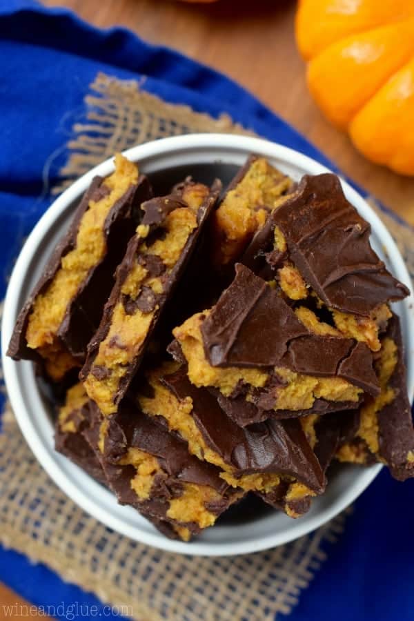 An overhead photo of the the Pumpkin Cookie Dough Bark in a ceramic bowl showing that the pumpkin cookie dough has chocolate chip cookies and wedged between two layers of melted chocolate. 