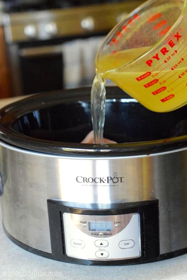 pour chicken stock from a measuring cup into a slow cooker to make chicken tacos