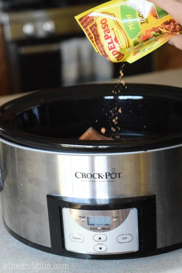 a packet of taco seasoning being poured into a slow cooker