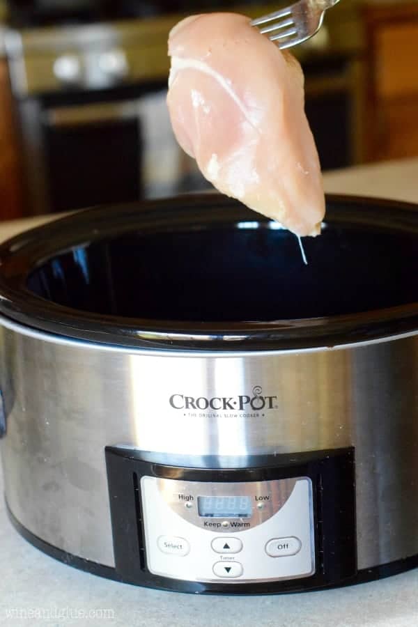 a raw chicken breast being placed into a crockpot to make tacos